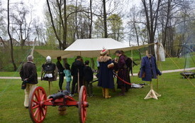 namiot z bronią, obok armata, ludzie przy stoisku