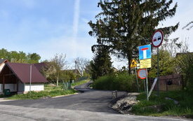 po lewej przystanek, obok droga asfaltowa , drzewo, znaki