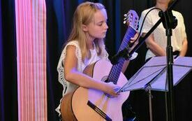 dziewczynka gra na gitarze, w tle Burmistrz