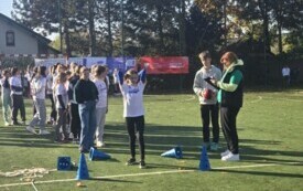 dziewczynka rzuca piłką, obok sędzia i chłopak, w tle inni zawodnicy