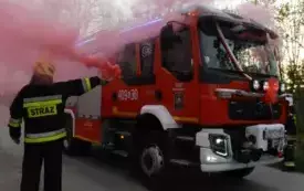 samoch&oacute;d strażacki, z lewej strażak z palącą się racą