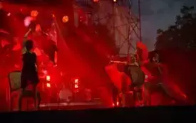 na oświwetlonej na czerwono scenie śpiewa piosenkarka i tańczą tancerki