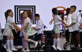 dzieci w kolorowych s&oacute;dniczkach tańczą na scenie