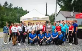 uczestnicy wydarzenia w pamiątkowej fotografii, w tle budynek, namiot, drzewa